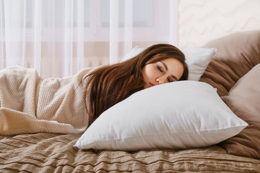 A woman sleeping peacefully on a soft white pillow, highlighting the connection between quality sleep and productivity, in a bright and calming bedroom with sheer curtains in the background.