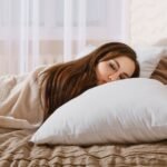 A woman sleeping peacefully on a soft white pillow, highlighting the connection between quality sleep and productivity, in a bright and calming bedroom with sheer curtains in the background.